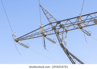 Metal framework of electricity pylon supporting high voltage power cables against a bright blue sky - Powered by Shutterstock