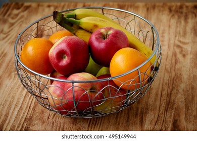 Metal fruit bowl on a wooden surface. Close. Bananas, oranges and apples