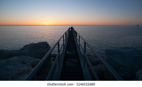 A Metal Gang Plank Juts Out Into The Water At Sunrise