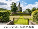 Metal gate, gardens and Veves Castle on hill against blue sky, towers with conical roofs and stone walls, huge tree with green leaves, sunny day in Houyet, Namur province, Wallonia, Belgium