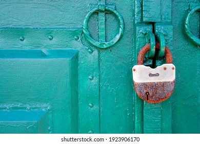 The metal gate is padlocked. Rusty padlock on the gate, close-up. Rough iron doors painted green.
