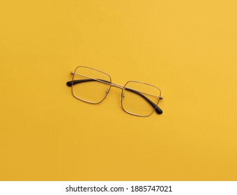 Metal Gold Eyeglasses In Square Frame, Transparent For Reading And Good Eye Sight, Top View Optical Glasses On Yellow Background