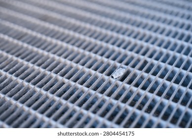Metal Grating With Narrow Rectangular Slots Showing Worn Paint And Small Debris In Urban Ground Surface Close-Up Industrial Texture And Pattern.