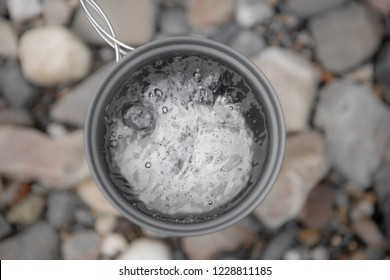 Metal Gray Mug With Boiling Water Close-Up On Background Of River Stones, Top View. Boiling Water In The Campaign.