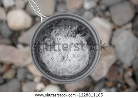 Metal Gray Mug With Boiling Water Close-Up On Background Of River Stones, Top View. Boiling Water In The Campaign.