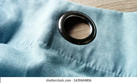 Metal Grommet On A Gray-blue Velvet Curtain. The Fabric Lies On A Wooden Table. The Hole On The Material Is Made Of Silver Coated Aluminum. Close-up Of A Metal Eyelet