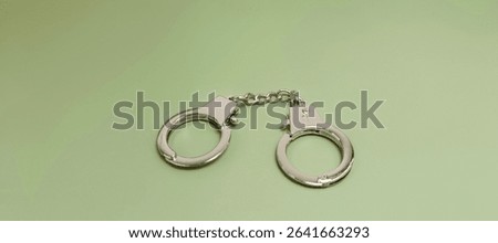 Metal Handcuffs on Green Background Representing Law Enforcement, Crime, Arrest, Police Tools, Legal Punishment, and Justice System in a Minimal Concept. 