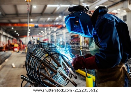 A metal and heavy industry worker processing armature with welder at factory.