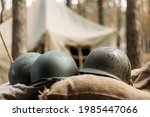 Metal Helmets Of United States Army Infantry Soldier At World War II. Helmets Near Camping Tent In Forest Camp.