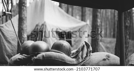 Metal Helmets Of United States Army Infantry Soldier At World War II. Helmets Near Camping Tent In Forest Camp. black and white photography