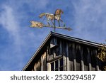 A metal horse weather vane arrow on a barn rooftop against with a sky background