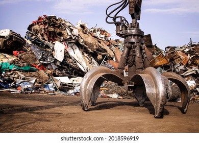 Metal junk yard with hydraulic lifting machine with claw attachment for scrap metal recycling.
