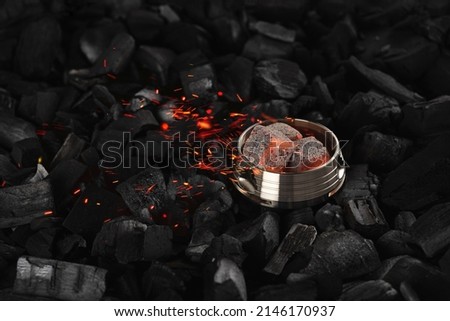 Metal kalaud hookah holder with burning coconut charcoal cubes and sparks on a black background. Horizontal orientation, copy space, no people. 