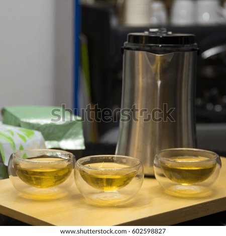 Metal kettle and green tea into chinese glass transparent bowls. Small cups of tea with iron teapot on marble table. Pials with double walls, double-bottomed bowls. Square