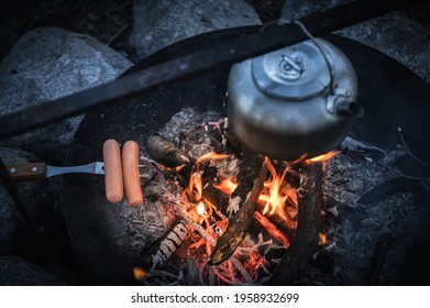 Metal kettle and grilled sausage on a campfire