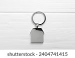 Metal keychain in shape of house on white wooden table, top view