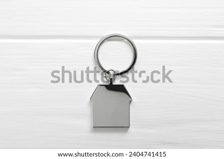 Metal keychain in shape of house on white wooden table, top view