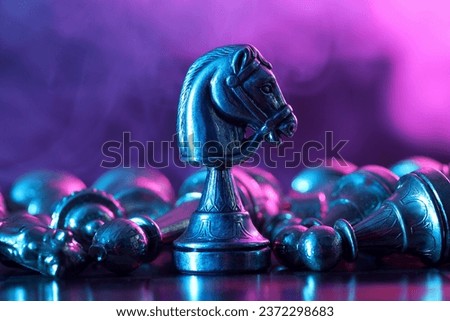 Metal knight among fallen chess pieces on checkerboard in color light, closeup