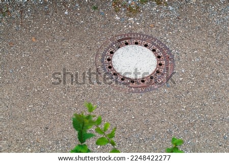 Metal manhole cover on a gravel walkway. The urban pavement drainage system. Old closed sewer manhole among the stones