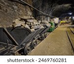 A metal mine cart filled with rocks on tracks inside a dimly lit underground mining tunnel