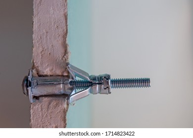 Metal Molly Fastener Fixed In A Pre-drilled Hole In A Sheet Of Moisture-resistant Drywall, Split View. The Sheet Is Cut At The Installation Site, Showing The Gypsum Fiber And Connection Details.