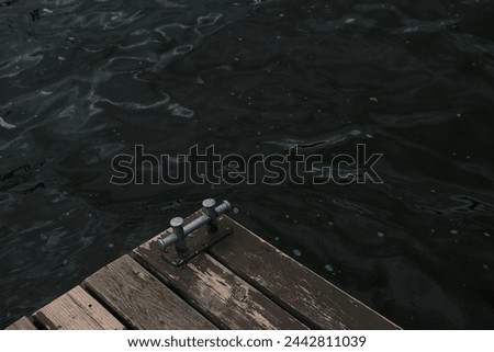 A metal mooring bollard and its shadow on an old wooden dock pier. Background. View from above.