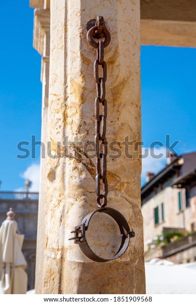 A metal neck iron on a pillory made of\
stone, which hangs down from a chain and where in former times\
prisoners were chained, who were put on the\
pillory