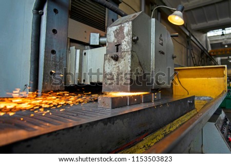 Metal parts on a flat grinder are treated with an abrasive wheel, sparks fly from under the circle, wide-angle photos