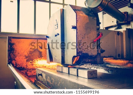 Metal parts on a flat grinder are treated with an abrasive wheel, sparks fly from under the circle, wide-angle photos. Toned photo.