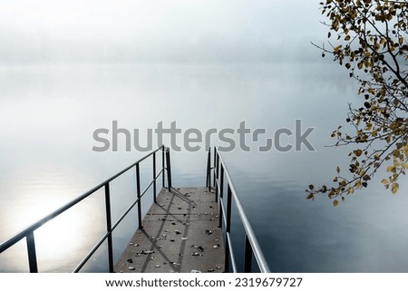 Metal pier to enter a lake, calm water with soft reflextion on a foggy autumn day. 