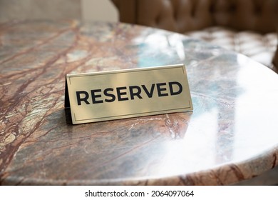 Metal Plaque With The Inscription Reserved On The Restaurant Stone Table.Reserved Sign With Capital Letters On The Dining Table In Restaurant, Cafe Or Office Center.