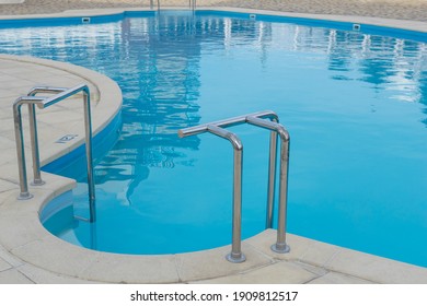 Metal Pool Ladder Handrails Of Swimming Pool With Blue Water, No People Around