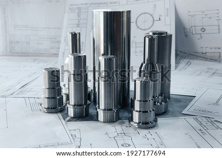 Metal products turned on a lathe lie on the drawings against the background of other drawings. Metalworking of products on CNC machines at the plant. 