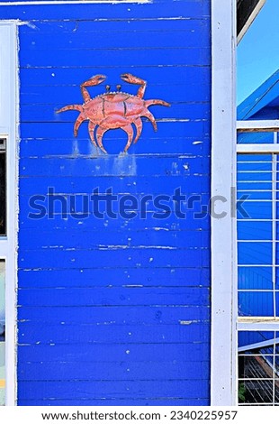 Metal red crab on bright blue wooden building with white window framing, copy space
