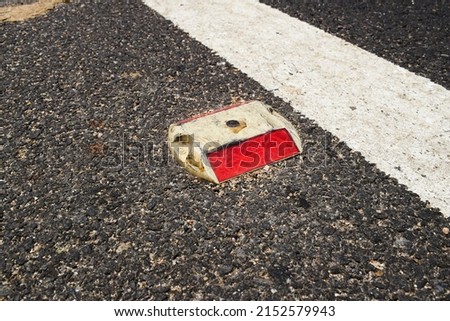 Metal Road stud with Red reflector on asphalt road with white painted lane marking line as divider on National highway road in India