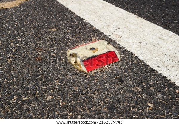 Metal Road stud with Red reflector on asphalt road\
with white painted lane marking line as divider on National highway\
road in India