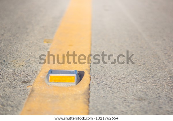 Metal road stud\
with yellow line on the\
road.