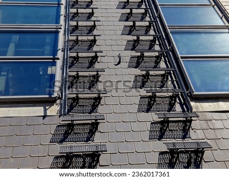metal roof steps on a pitched roof. roof windows. gray slate. the chimney sweep here throws the chimney for inspection. aerials and air conditioning exchangers