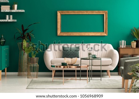 Metal, round coffee tables and a beige sofa in a green, luxurious living room interior with marble shelves and golden decorations