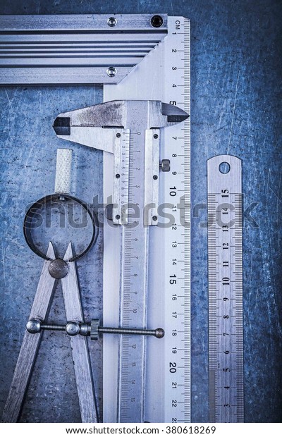 Metal ruler try square slide caliper\
construction pair of compasses on metallic\
background.