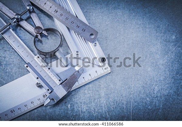 Metal ruler try square trammel\
caliper construction pair of compasses on metallic\
background.