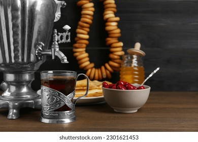 Metal samovar with cup of tea and treats on wooden table
