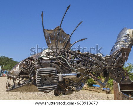 Metal sculpture of fish made of details of old cars (part of sculpture of robot/knight in boat). Camp of bikers. Russia