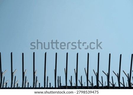 Metal security fence designed with sharp, upward-pointing spikes. The spikes, set against a bright blue sky, emphasize the boundary.