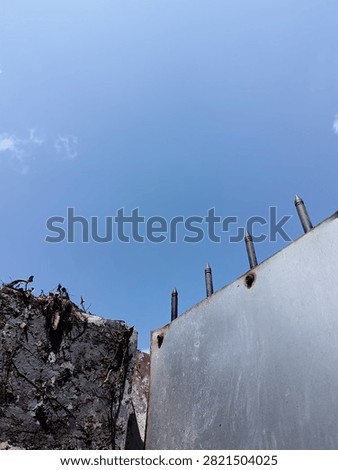 A metal security gate with sharp iron spikes stands beside a textured concrete wall against a bright blue sky