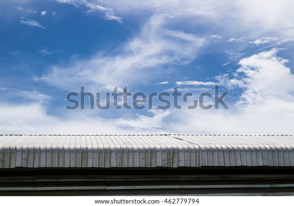 Metal sheet roof\
building with blue sky background. Steel top part of warehouse or\
industrial construction.