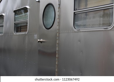 Metal side of vintage airstream travel trailer with circle window on the door.