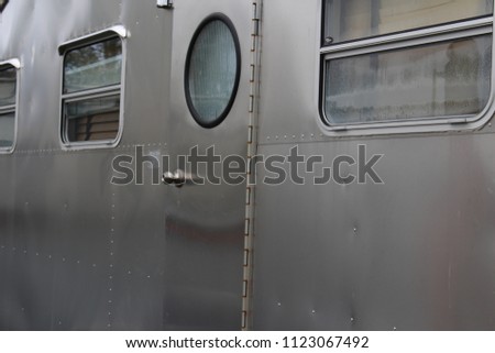 Metal side of vintage airstream travel trailer with circle window on the door.