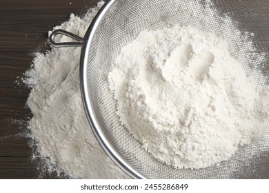 Metal sieve with flour on wooden table, top view