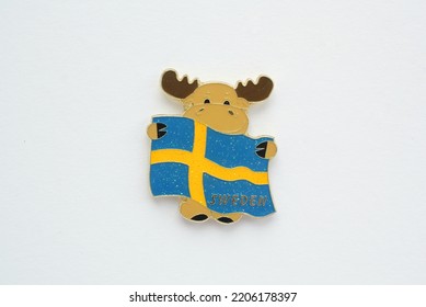 Metal Souvenir Fridge Magnet Of Moose Flag Sweden Isolated On White Background. Travel Memory Concept. Gift Typical Product For Tourist From Foreign Trip. Home Decoration. Top View, Flat Lay, Close Up